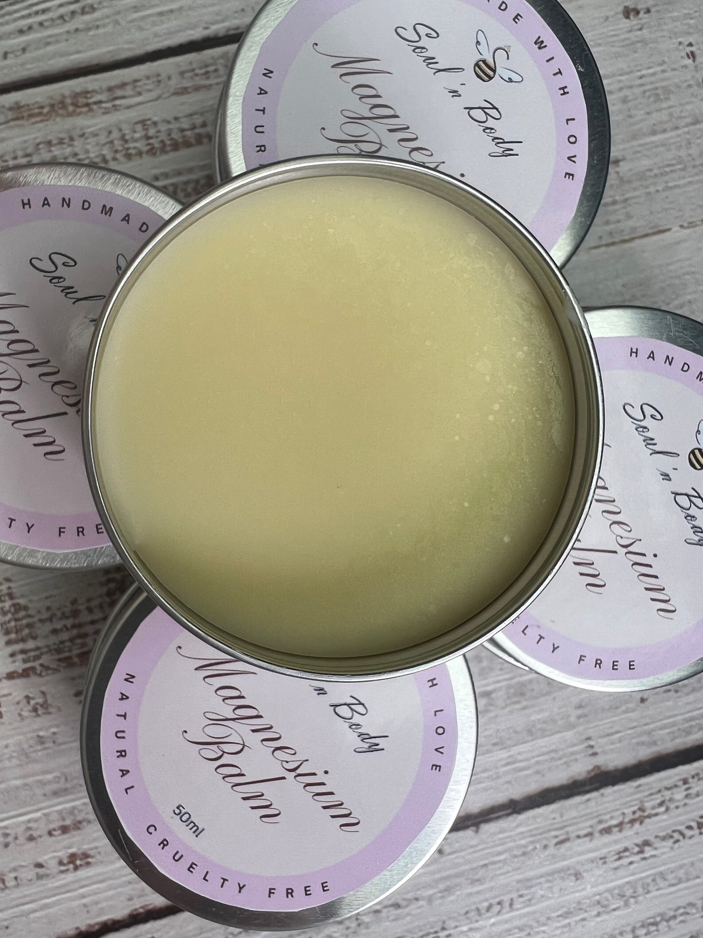 Balm in a metal tin surrounded by Soul & Body' containers on a wooden surface