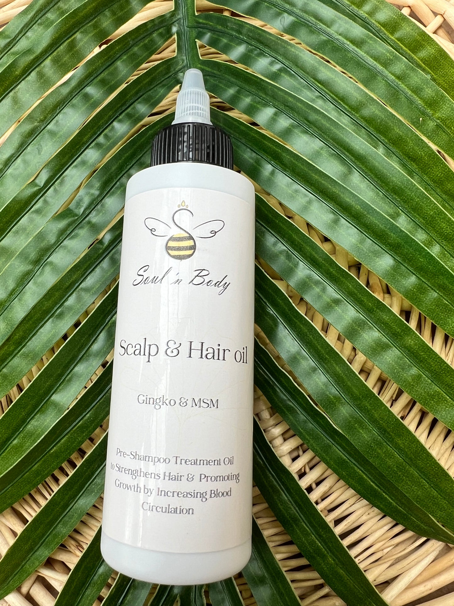 Bottle of Soul n Body Pre-Shampoo Hair & Scalp Oil placed on large green palm leaves.