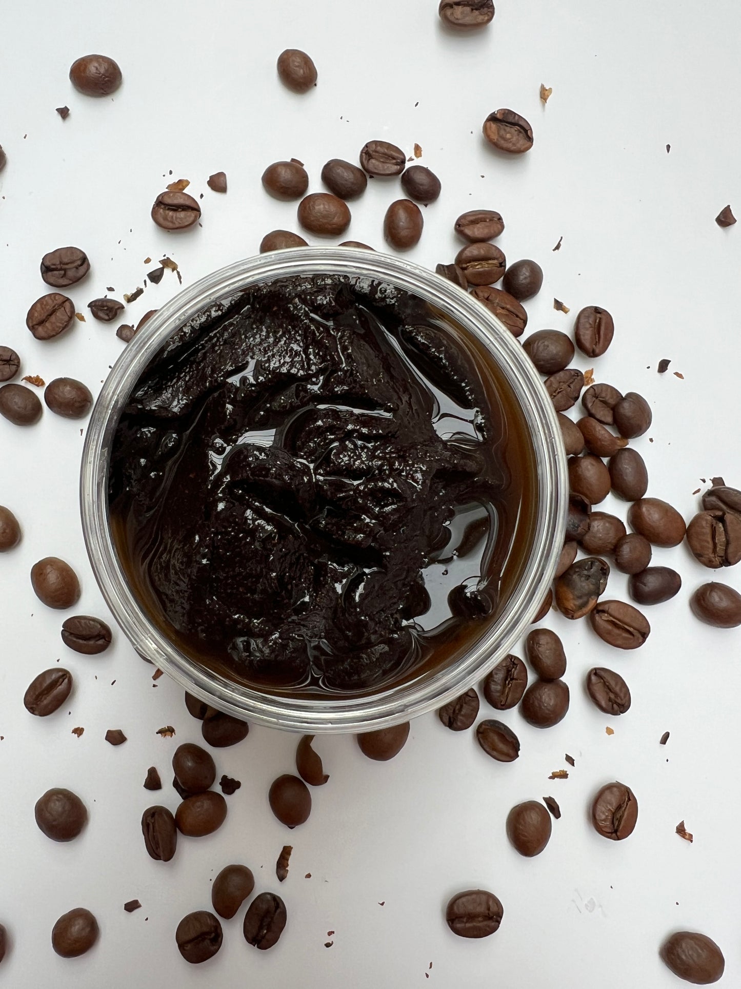 Coffee Scrub in a small container surrounded by coffee beans on a white background