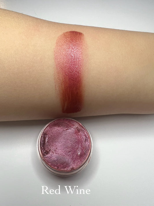 Red Wine – “Handmade deep red lip balm in a tin with a glossy swatch on skin, labeled Red Wine.