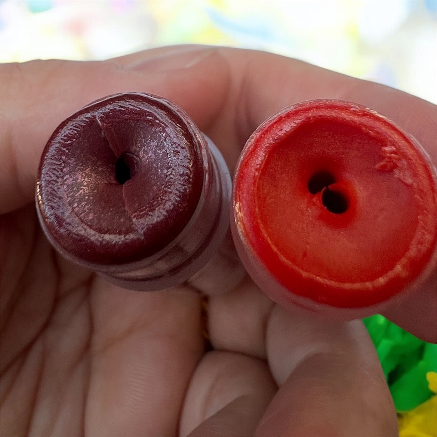 Top view of two lip balms — one deep berry, one coral red, showing smooth texture inside tubes.