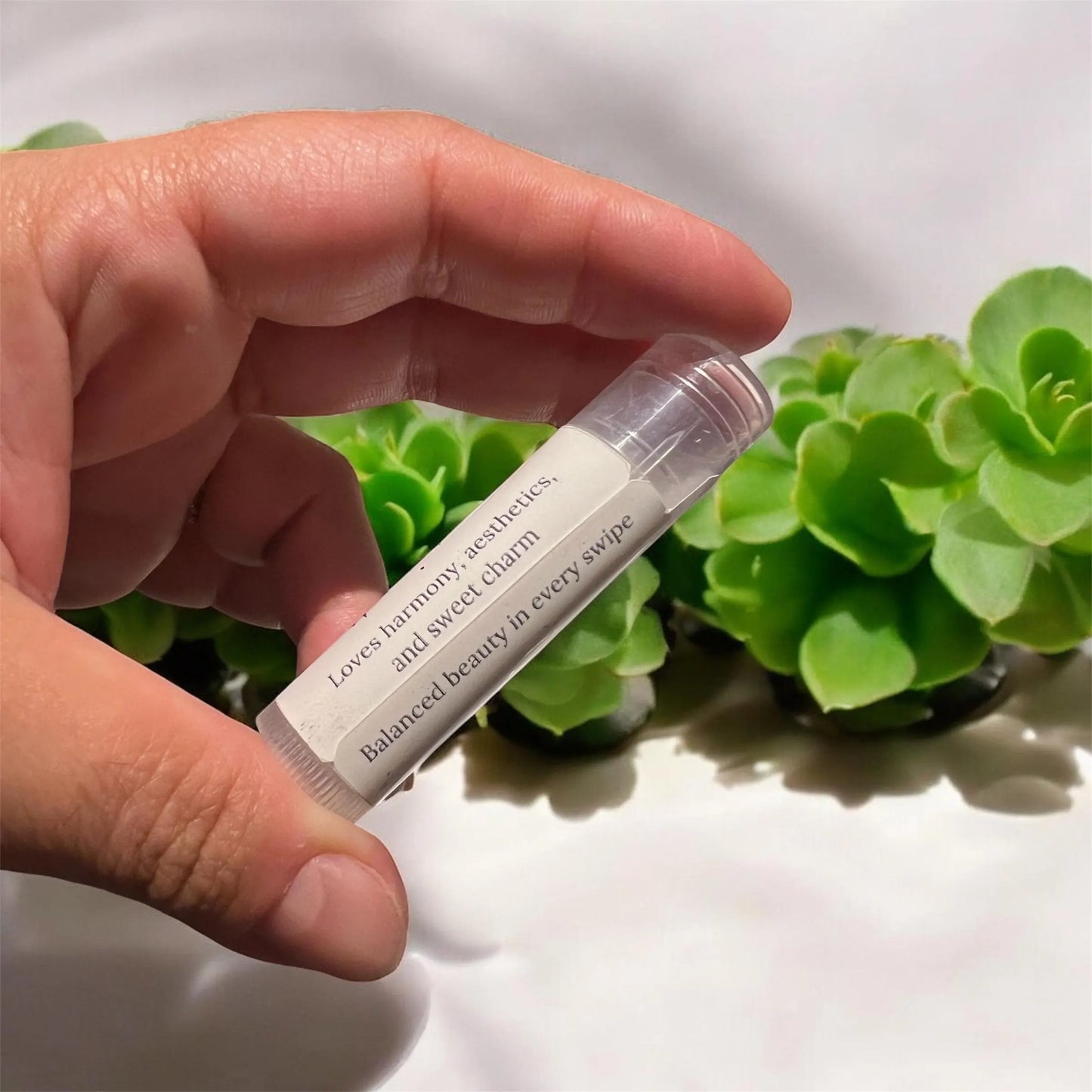 Hand holding zodiac lip balm tube against green leaves background