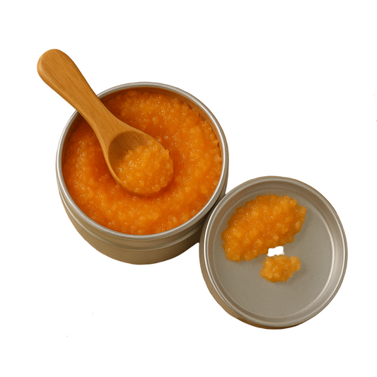 Jar of orange spread with a wooden spoon, grapes, and an orange slice on a beige cloth.