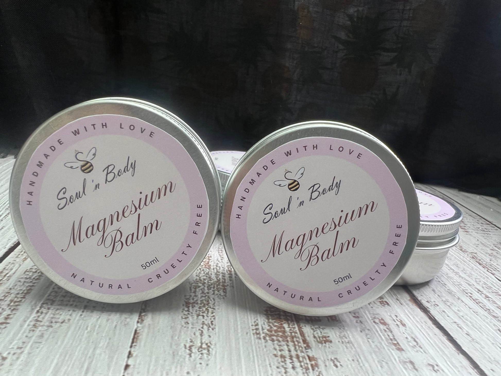 Two tins of Magnesium Balm with a visible brand logo on a wooden surface.