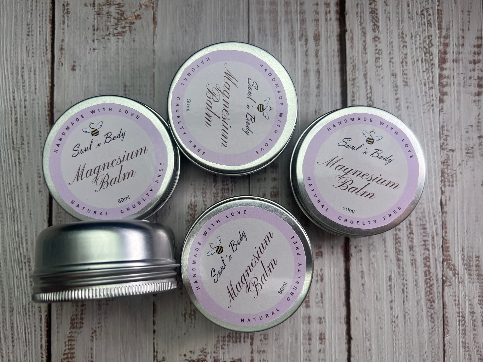 Four tins of magnesium balm with purple labels on a wooden surface