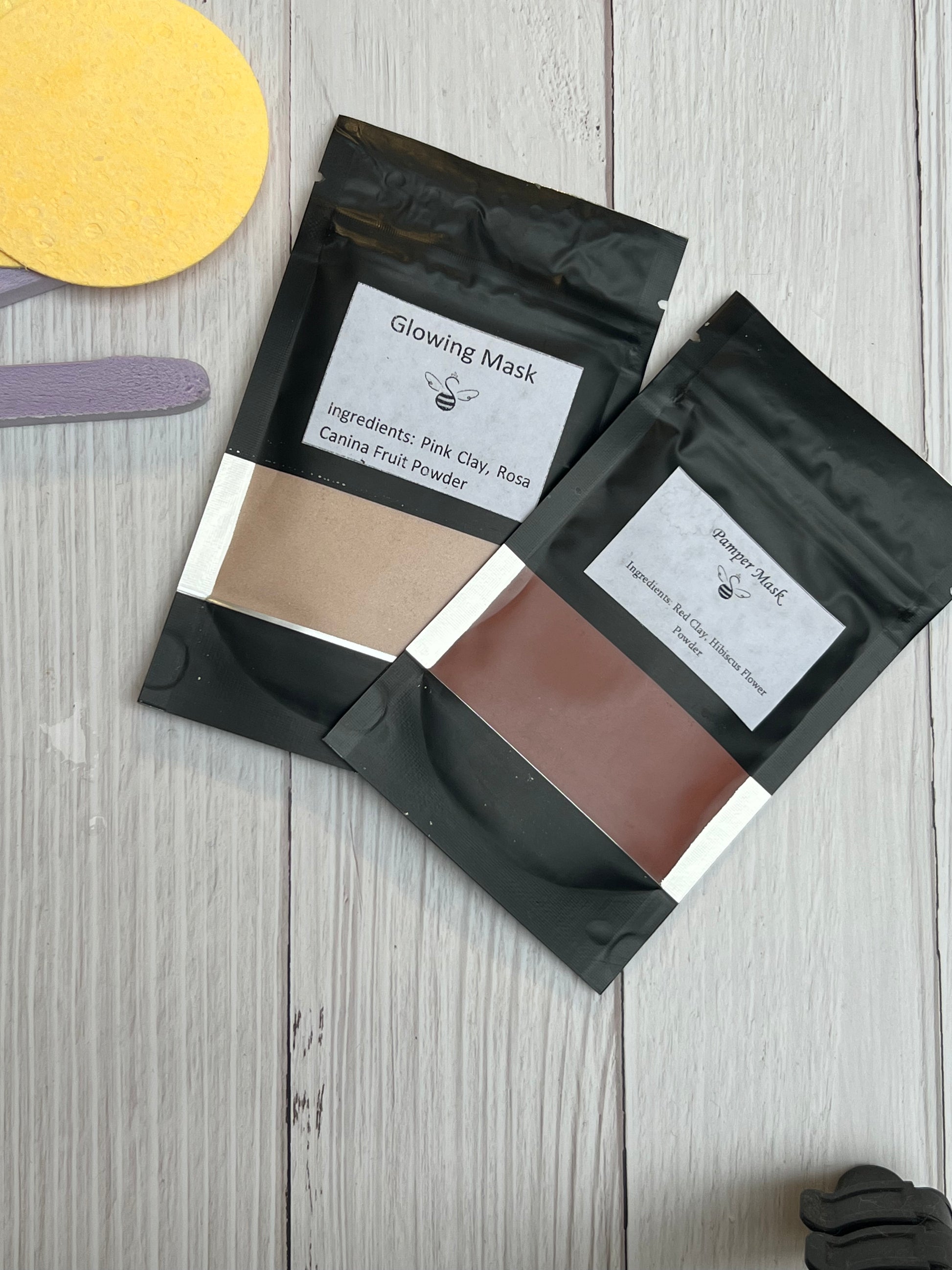 Several black resealable pouches of skincare powder masks displayed neatly, each with white labels, placed on a light wooden surface with one yellow round object partially visible.