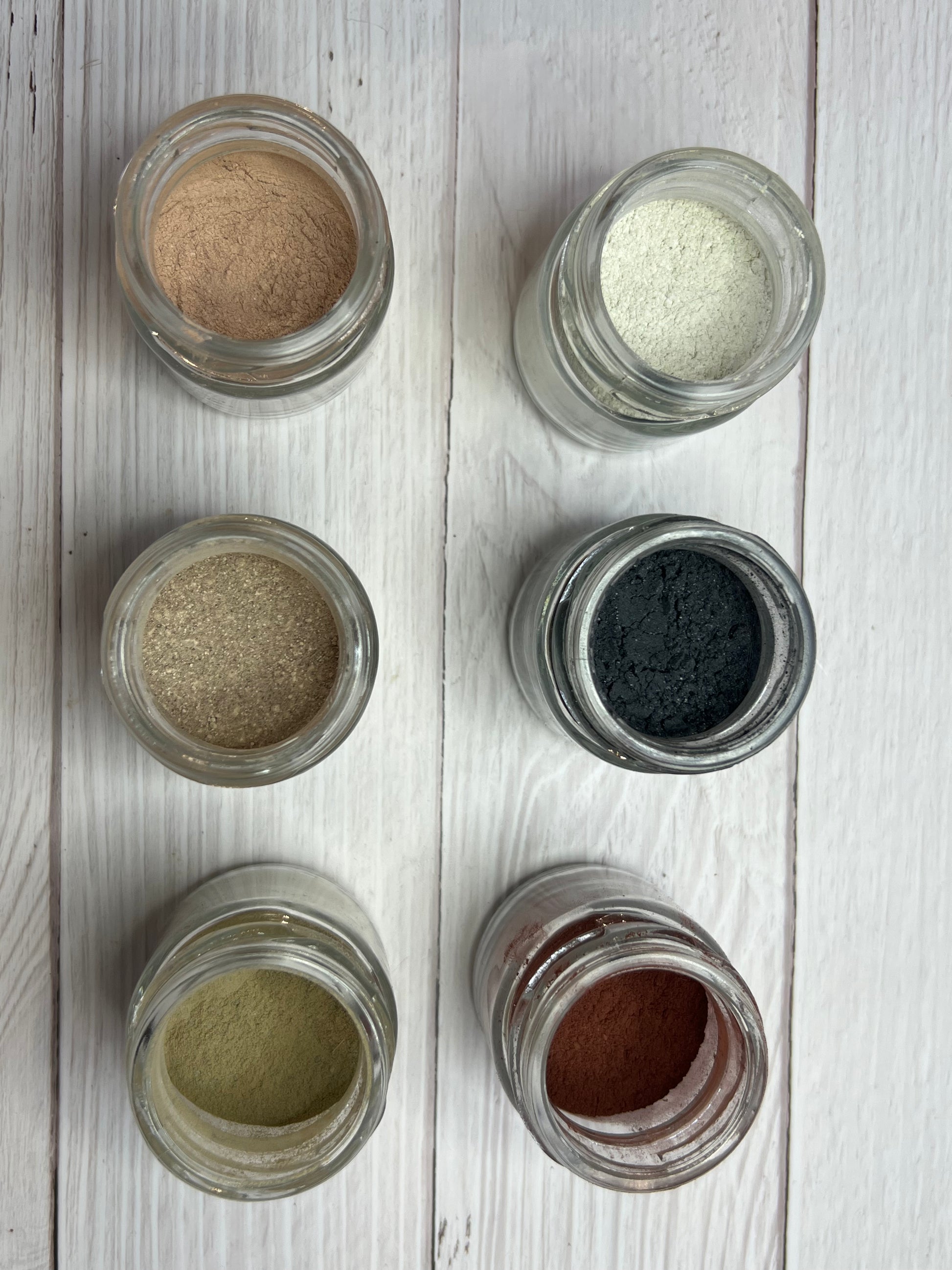 Flat lay of glass jars filled with natural green clay and cucumber powder face mask, displayed in a neat grid for a clean skincare presentation.