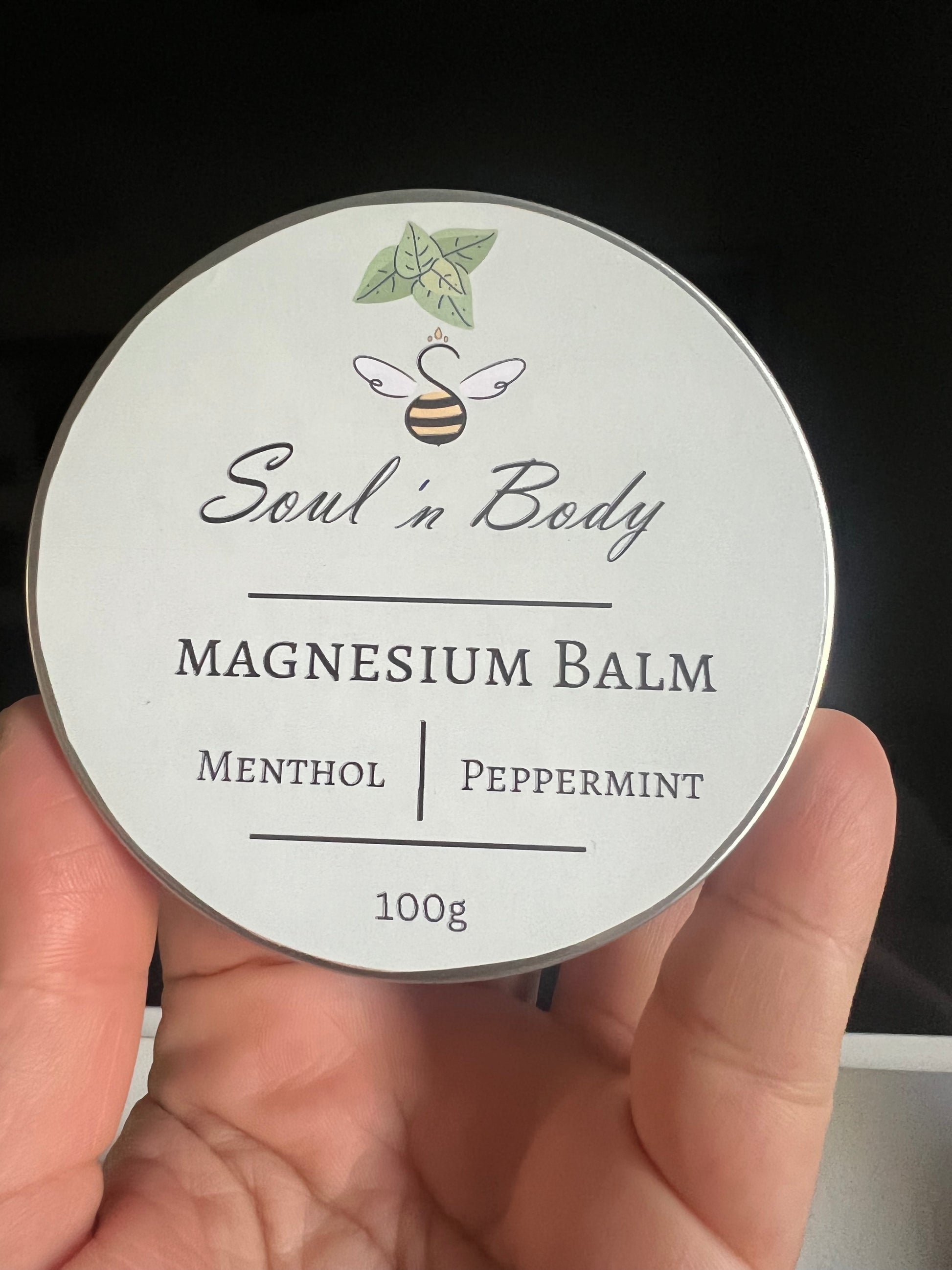 Soul 'n Body magnesium balm container held in a hand with a dark background
