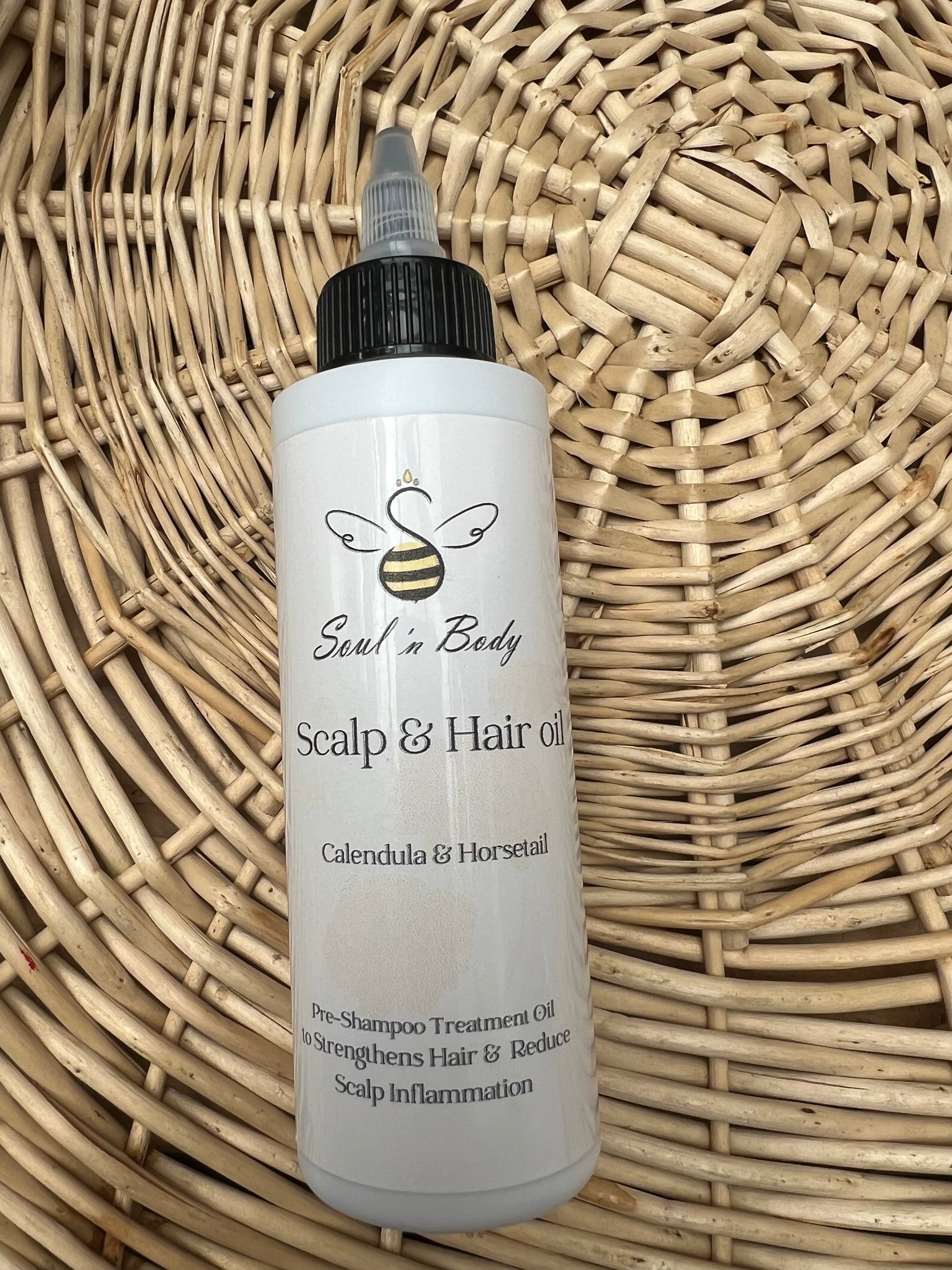 Close-up of a single Soul ‘n Body Calendula Horsetail Scalp & Hair Oil bottle on a woven basket background.
