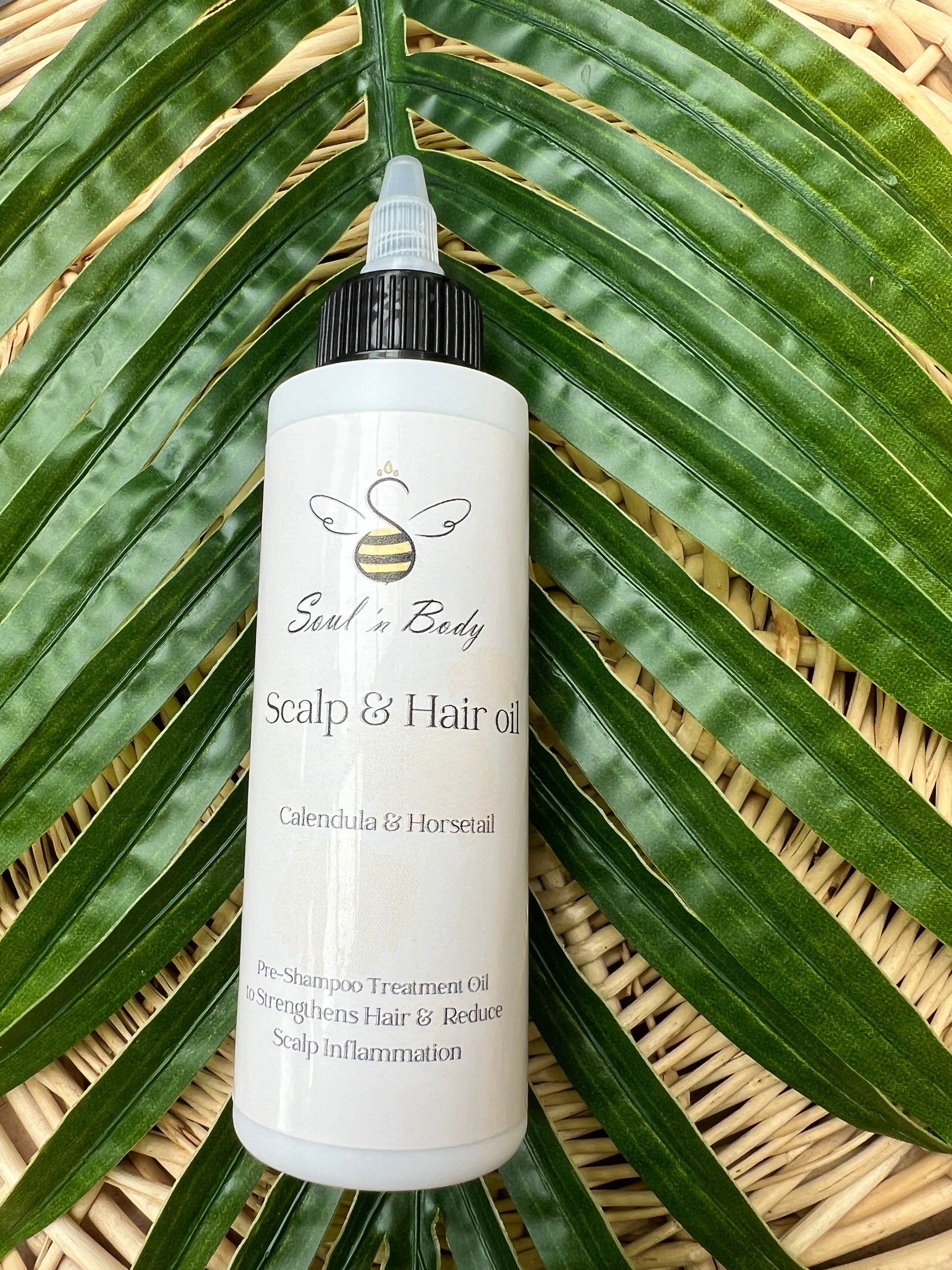 Bottle of Scalp & Hair oil on a leafy background with calendula and horsetail