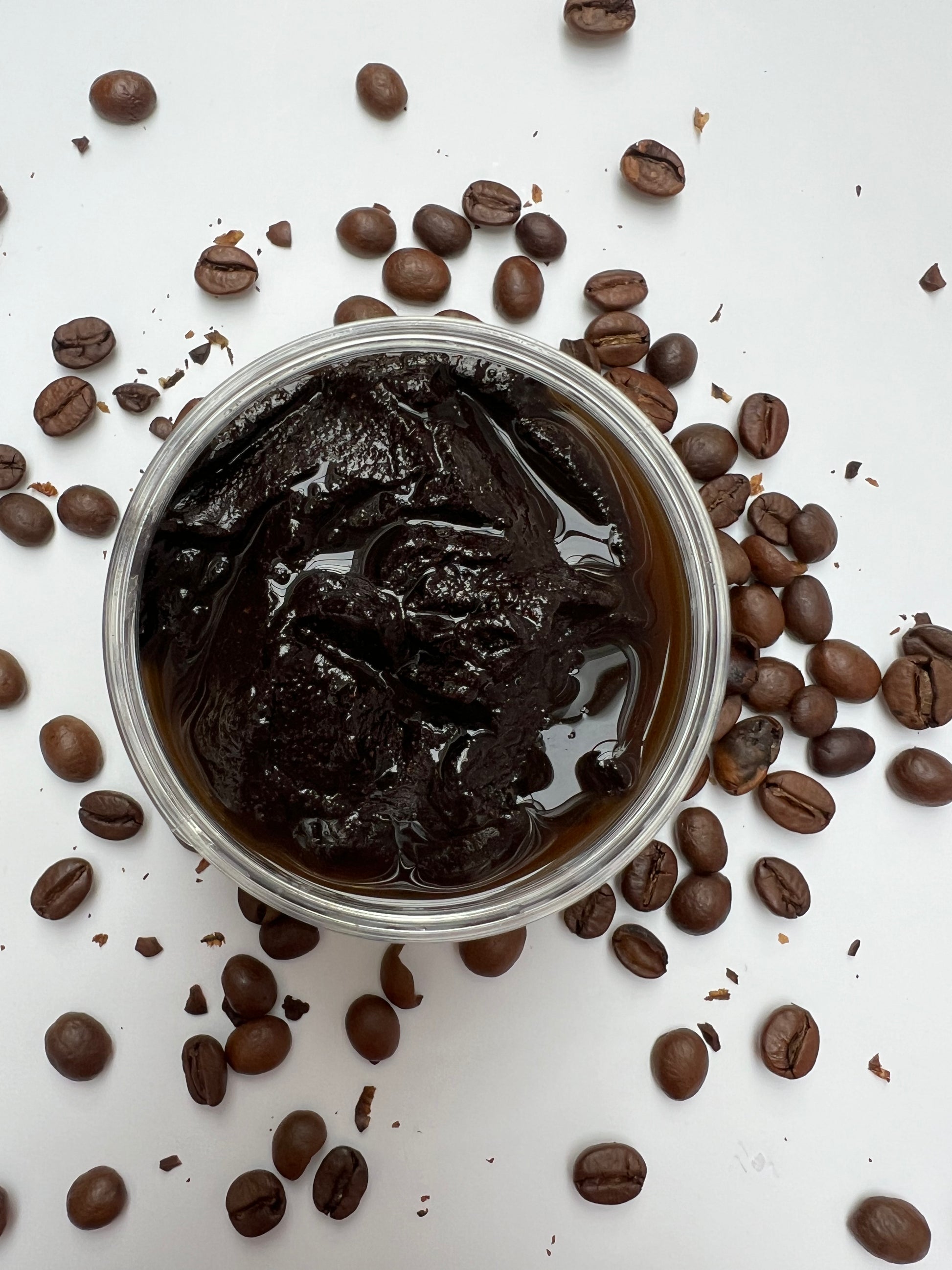 Coffee Scrub in a small container surrounded by coffee beans on a white background