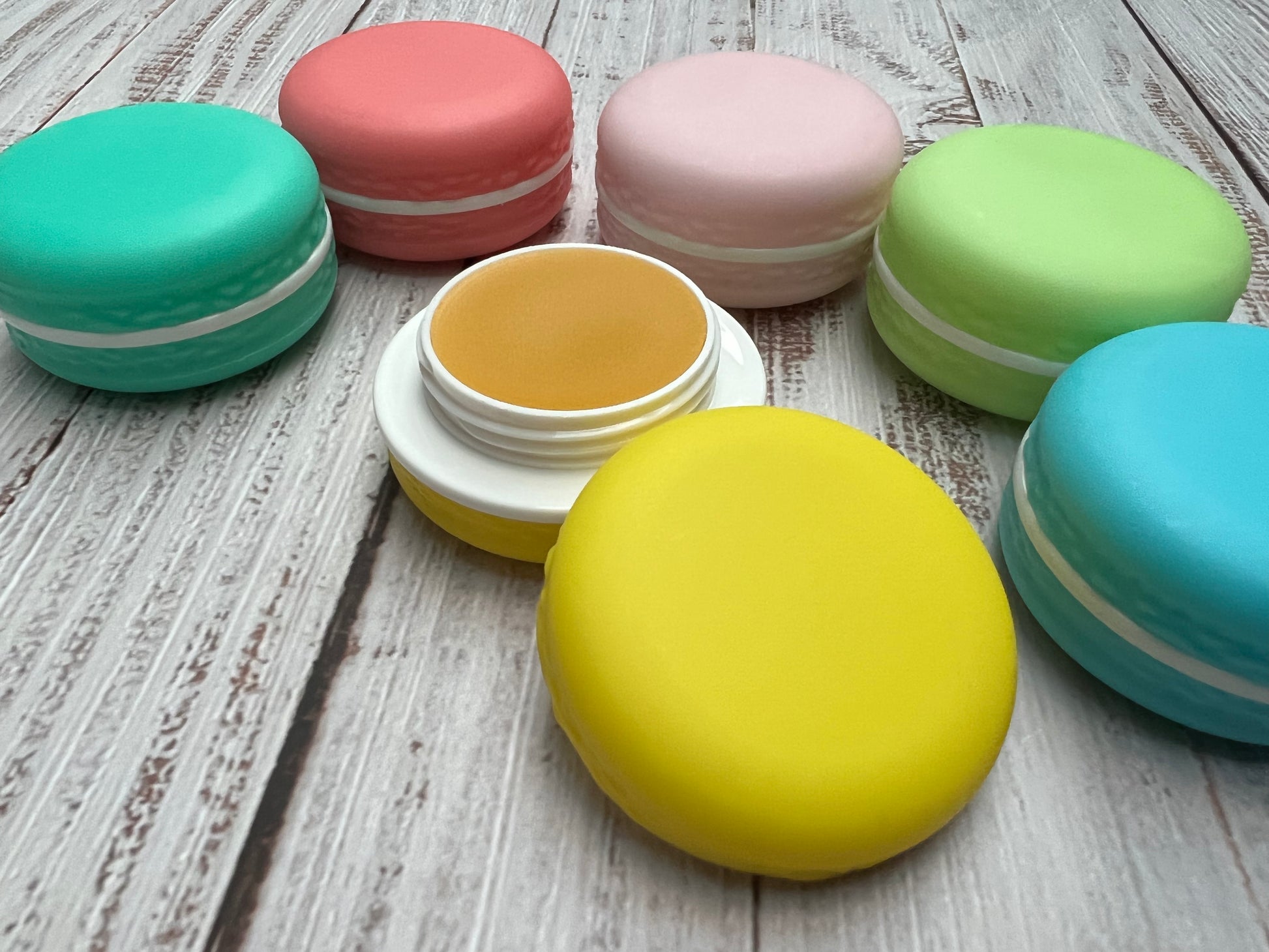 Pink and turquoise macaron lip balm pots stacked together, with the top pot open to show the balm.