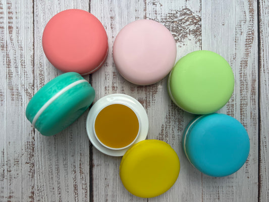 Set of closed macaron lip balm pots in pink, green, yellow and blue stacked neatly on a wooden surface.