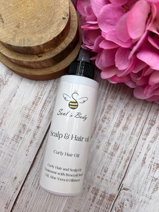 Bottle of Scalp & Hair Oil by Soul n' Body on a wooden surface with pink flowers.