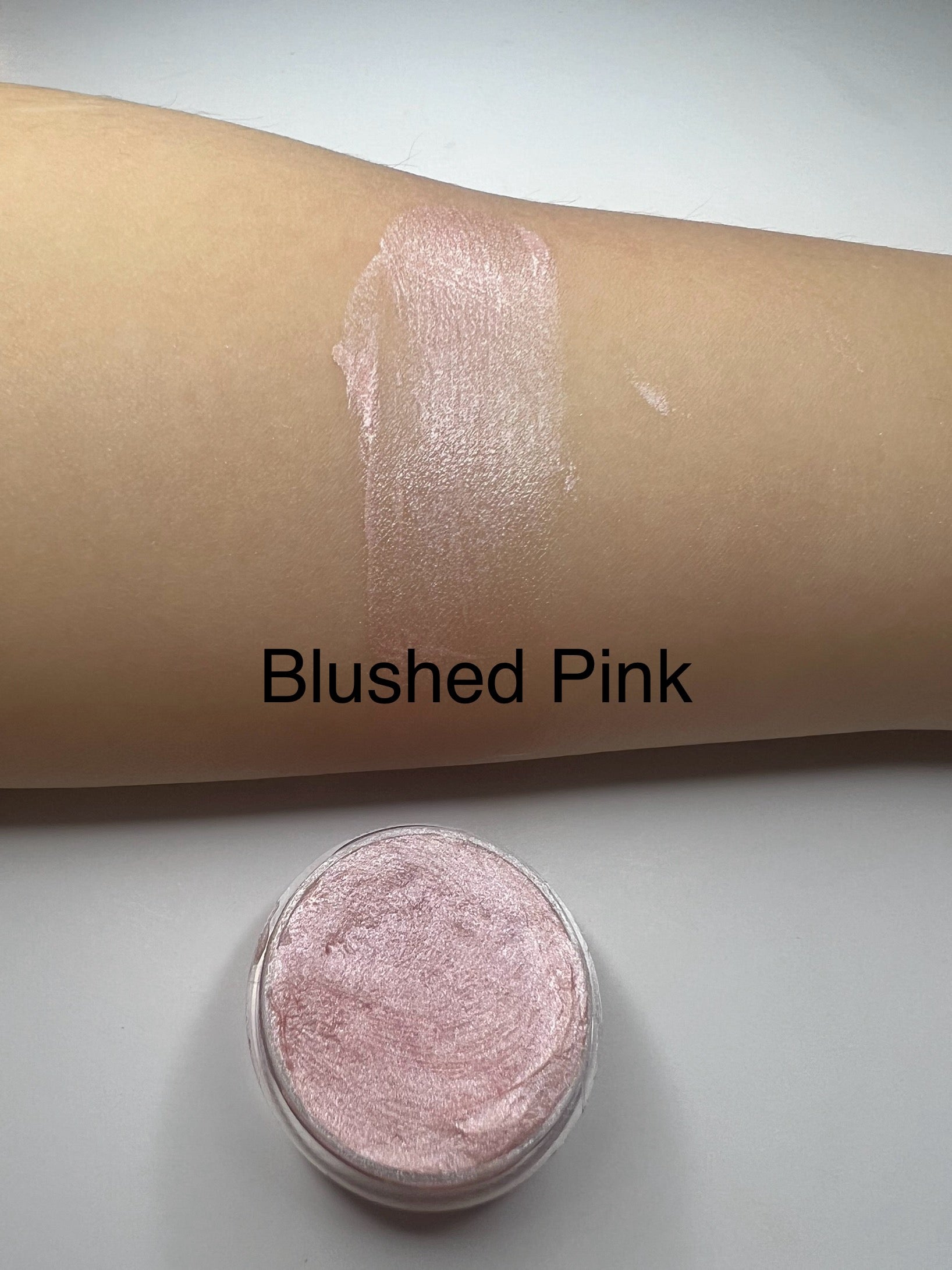 Blushed Pink – “Handmade pale blush pink shimmer lip balm in a tin with a swatch on skin, labeled Blushed Pink.