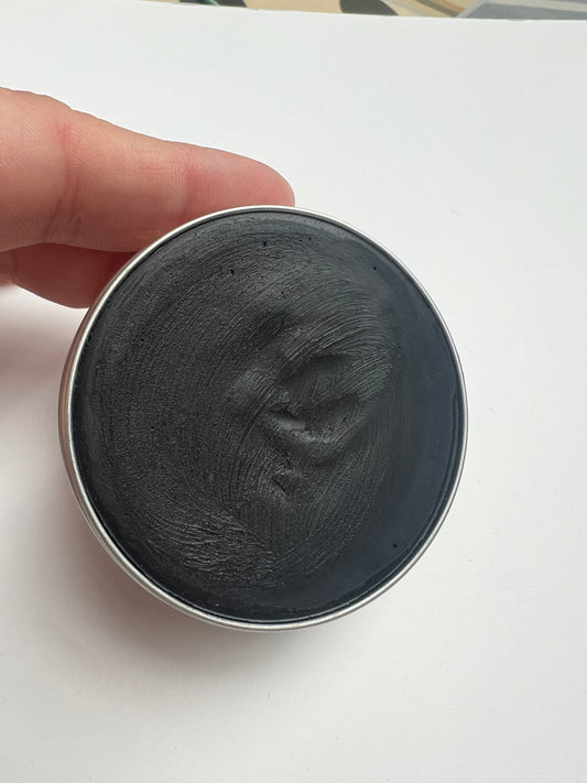 Open tin of natural activated charcoal deodorant held in hand against a white background.