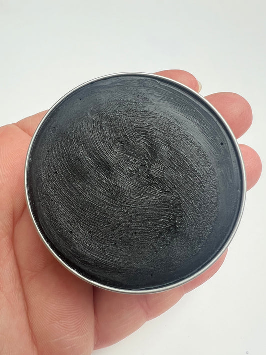 Open tin of natural activated charcoal deodorant held in hand against a white background.