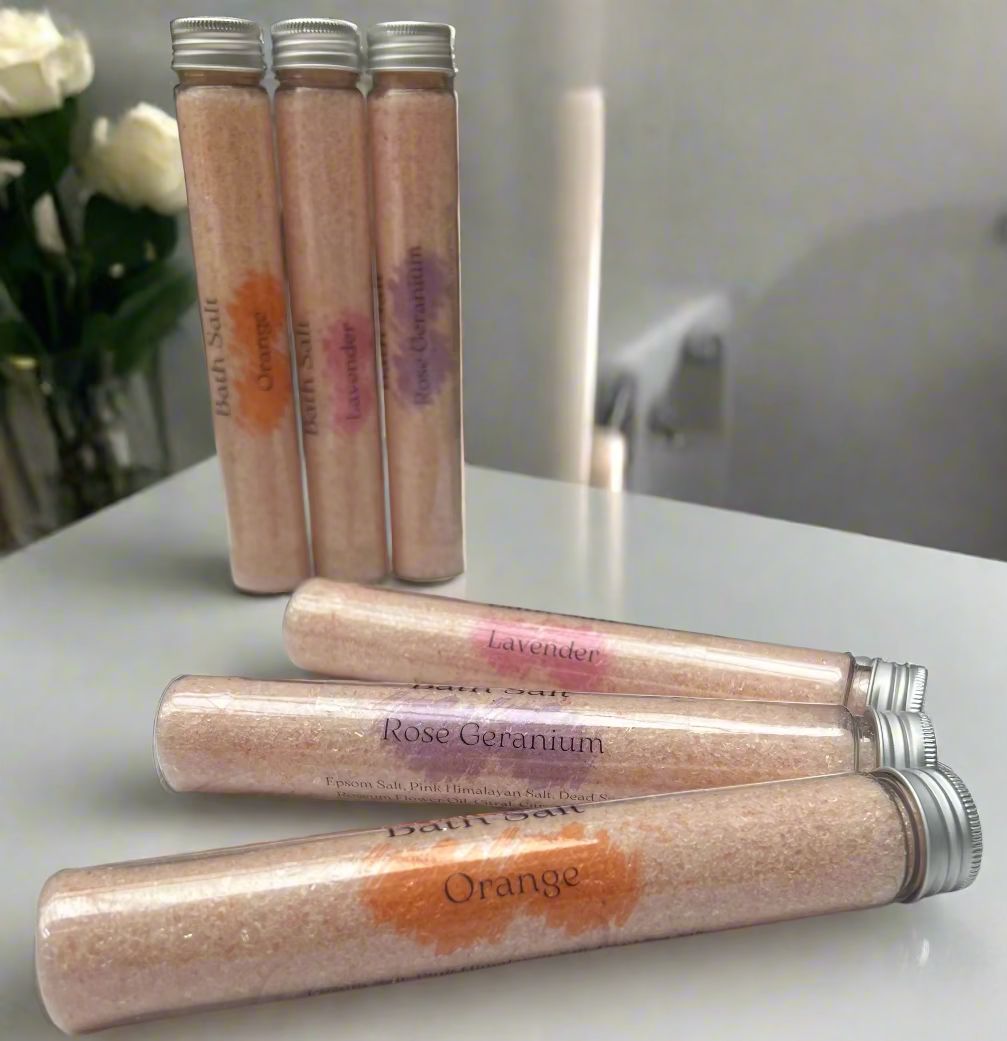 Stacked lavender bath salt tubes with cork stoppers on a light wood surface.