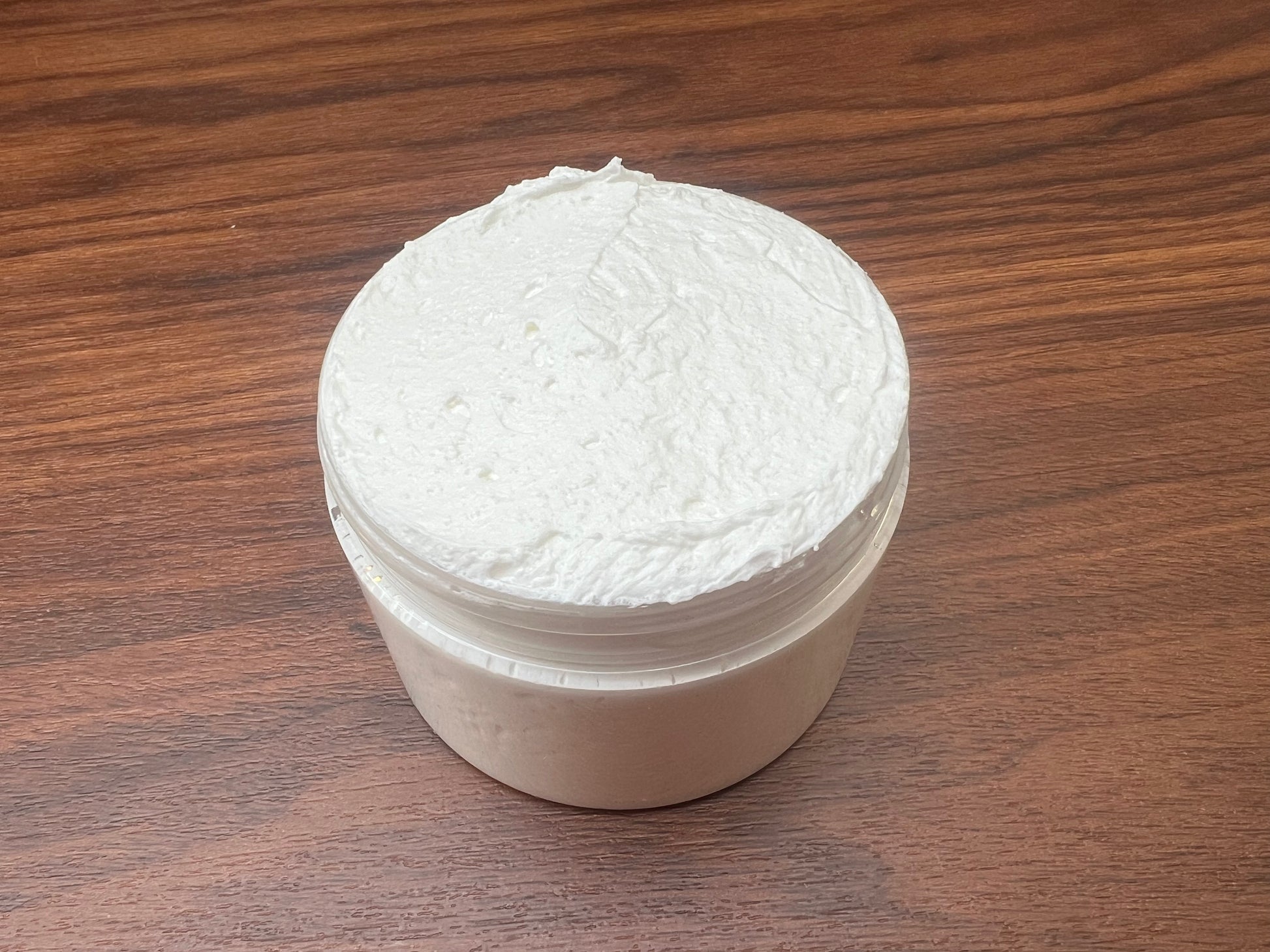 Top view of a jar filled with smooth, whipped body butter on a wooden surface.