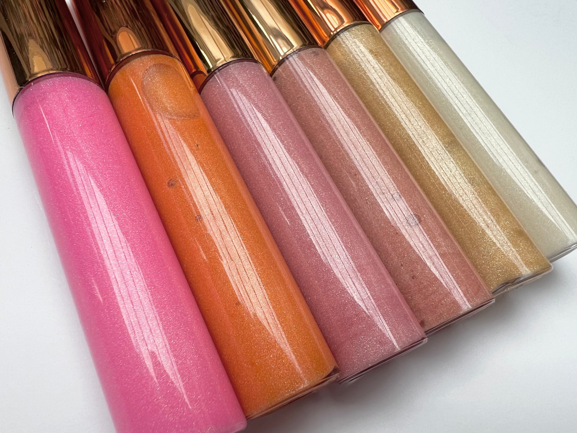 Set of 6 handmade natural lip glosses – bright and neutral shades including pink, peach, nude, and gold – moisturizing glossy finish.