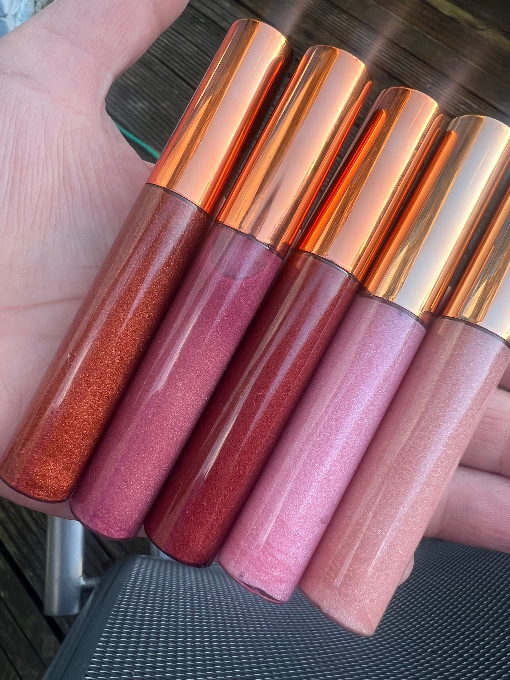 Set of four handmade lip gloss tubes in pink, nude, and red tones with rose-gold caps.