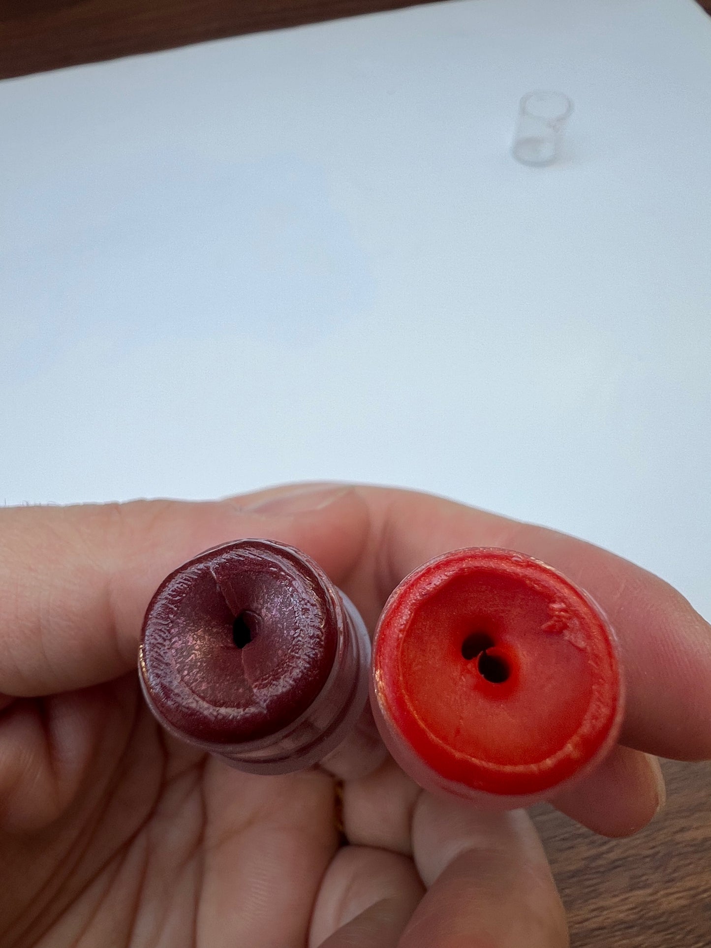 Top view of two lip balms — one deep berry, one coral red, showing smooth texture inside tubes.