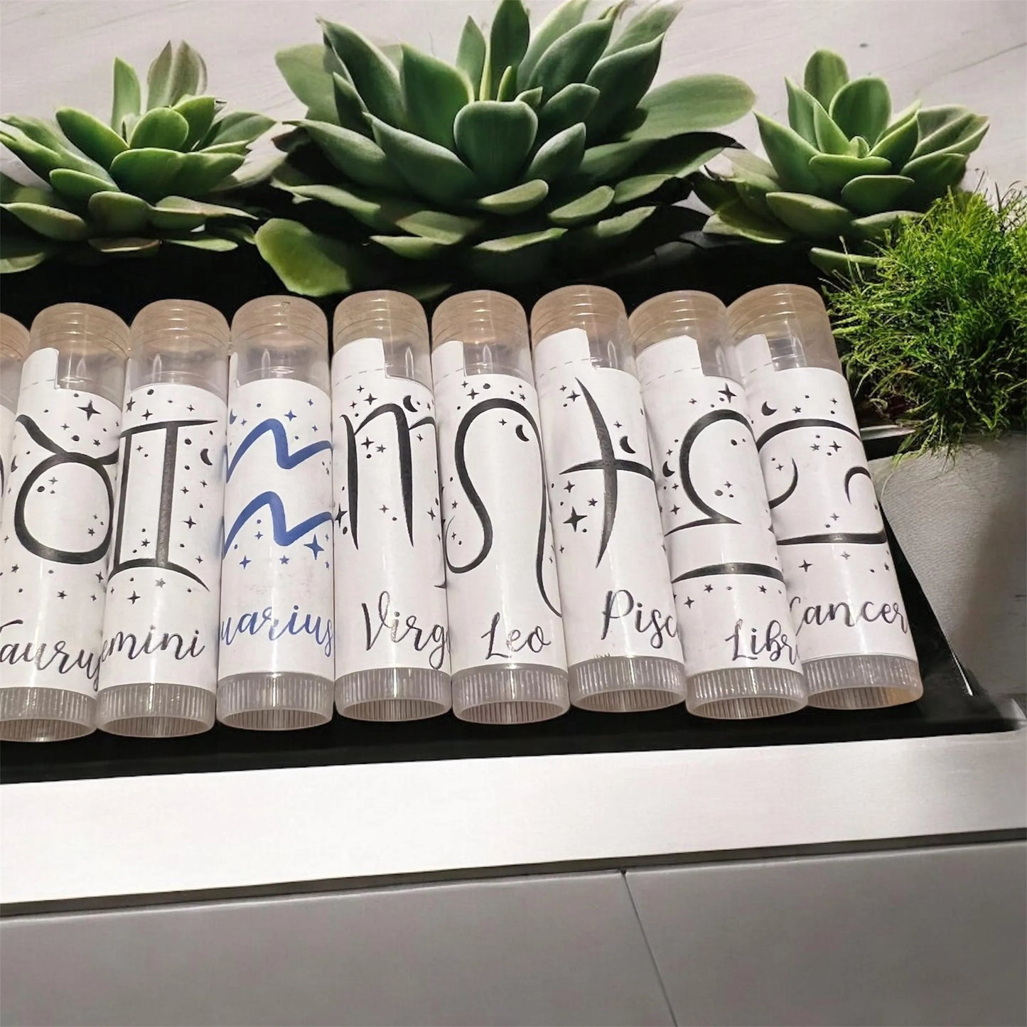 Vegan natural zodiac lip balms arranged with green leaves for eco-friendly presentation